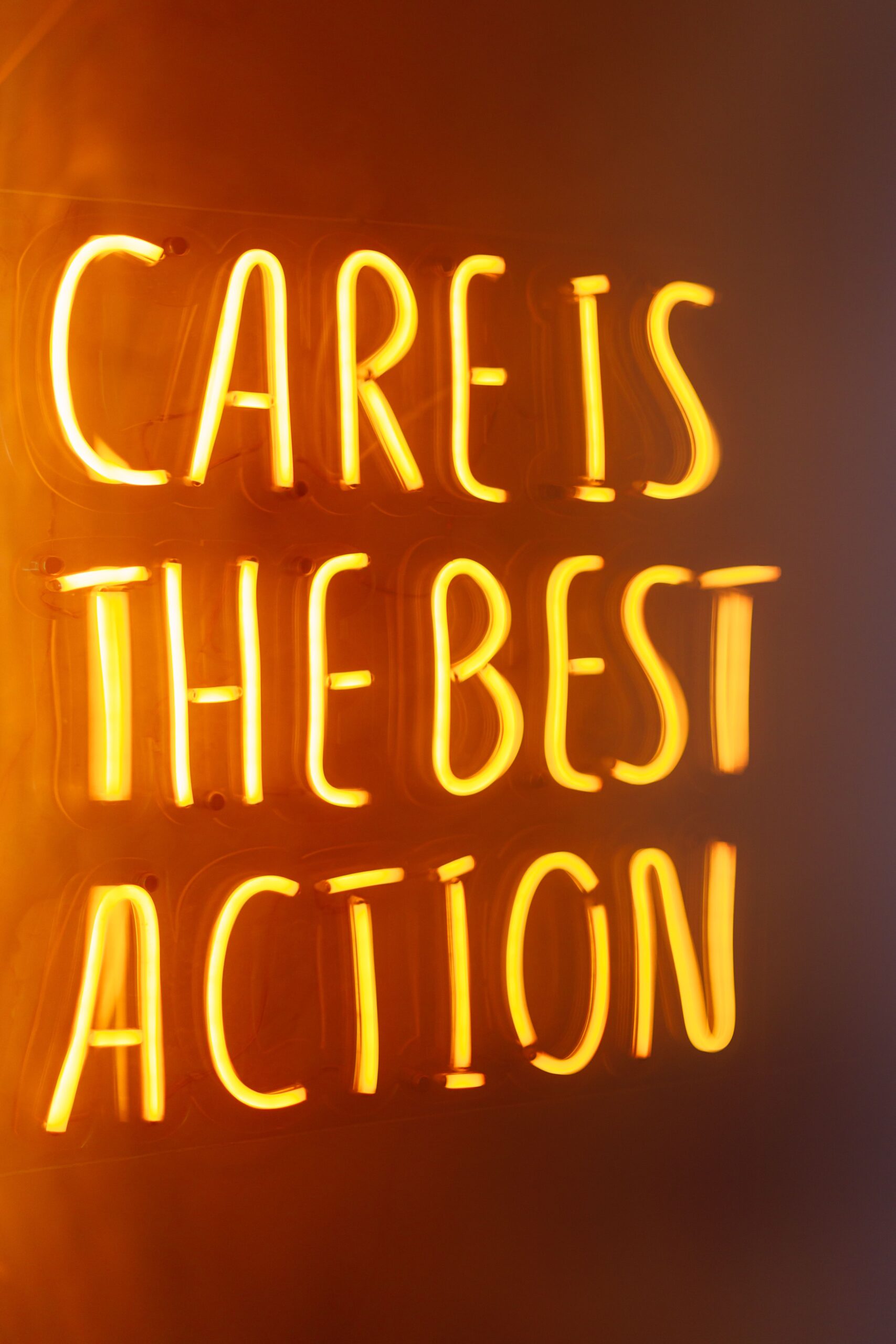 Bright neon sign reads 'Care is the best action,' glowing warmly on a vertical surface.